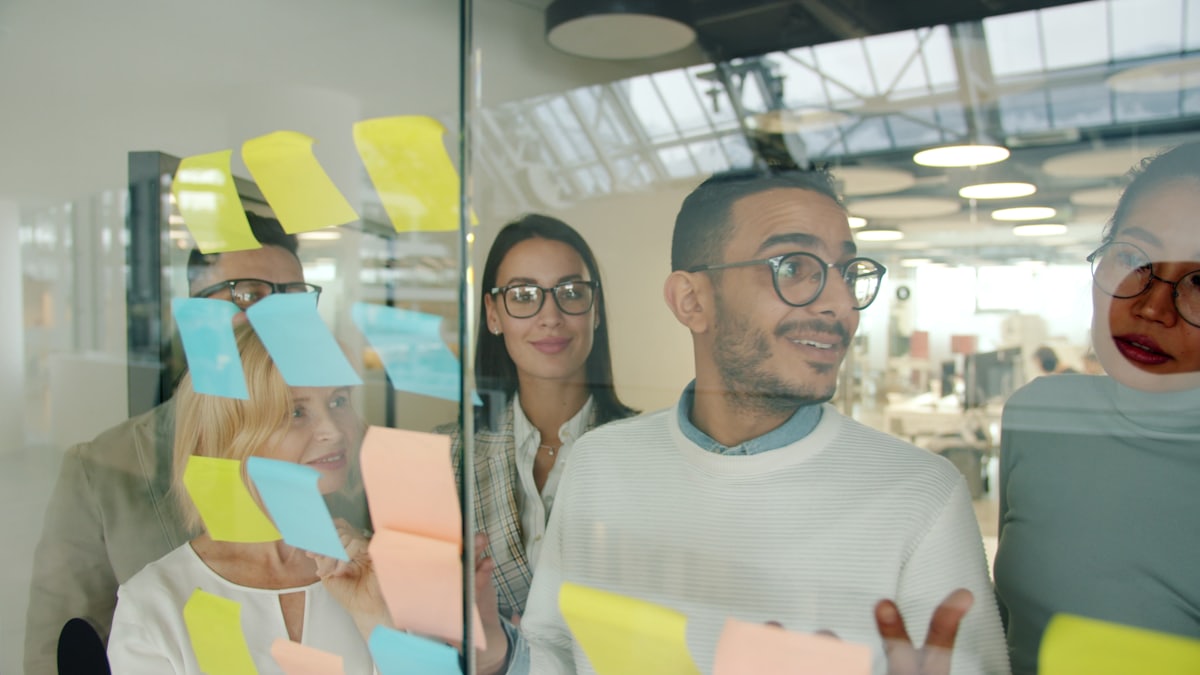 A multicultural group brainstorming with sticky notes on a glass wall.